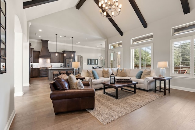 living room featuring beam ceiling, a notable chandelier, light wood finished floors, high vaulted ceiling, and baseboards