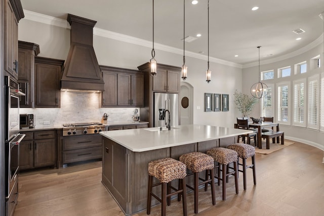 kitchen with arched walkways, stainless steel appliances, light countertops, custom range hood, and a large island with sink