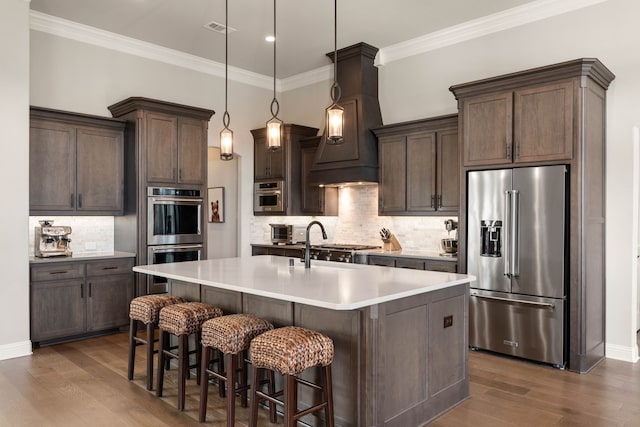 kitchen featuring dark wood-style floors, appliances with stainless steel finishes, a kitchen island with sink, light countertops, and pendant lighting