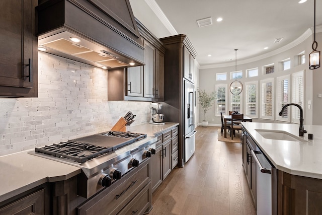 kitchen featuring appliances with stainless steel finishes, light countertops, premium range hood, pendant lighting, and a sink