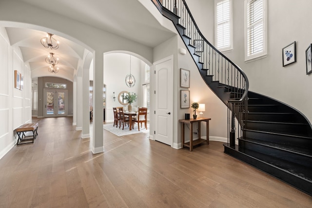 entrance foyer with arched walkways, stairway, an inviting chandelier, and wood finished floors