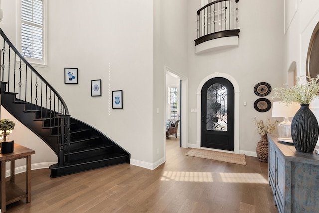 entryway featuring arched walkways, wood finished floors, a towering ceiling, and baseboards