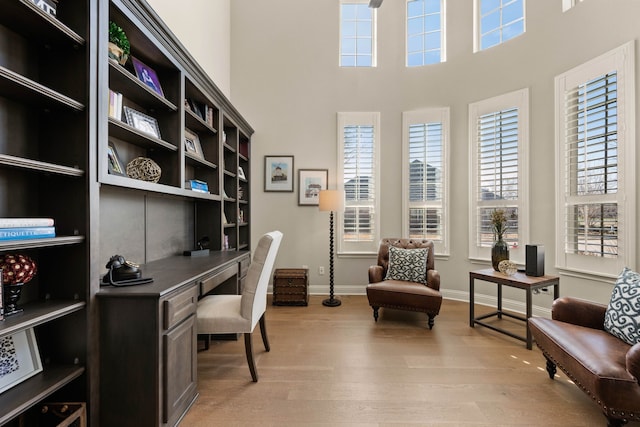 home office with light wood-type flooring, a towering ceiling, and baseboards