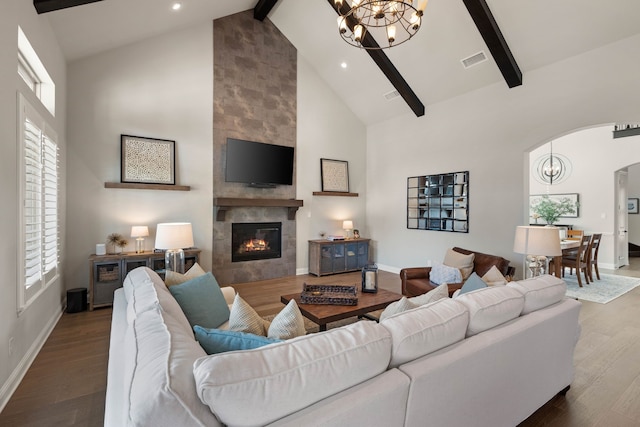 living area featuring arched walkways, visible vents, a tiled fireplace, an inviting chandelier, and wood finished floors