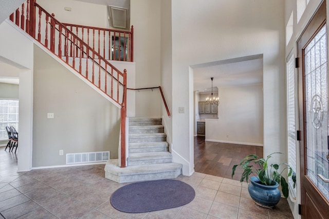 entryway featuring visible vents, a towering ceiling, stairway, an inviting chandelier, and tile patterned flooring