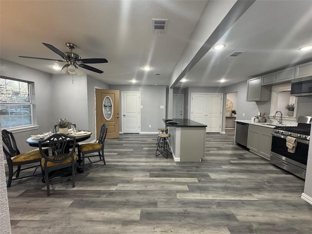 kitchen with a center island, stainless steel appliances, gray cabinets, visible vents, and a kitchen bar