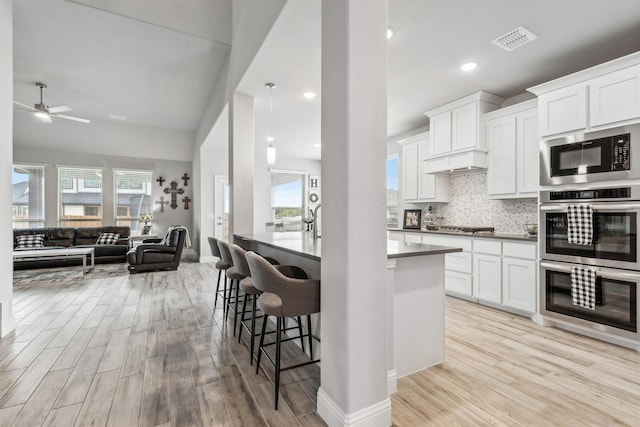 kitchen featuring visible vents, white cabinets, appliances with stainless steel finishes, open floor plan, and light wood-style floors