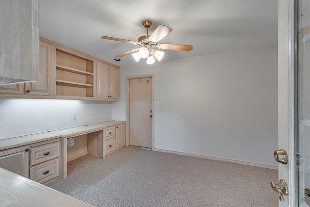 unfurnished office with baseboards, a ceiling fan, built in desk, and light colored carpet