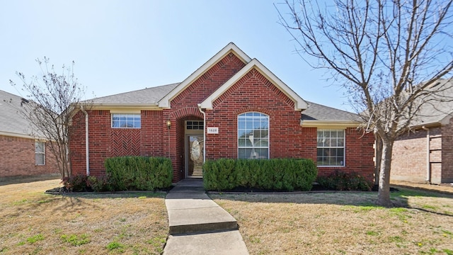 view of front of property featuring a front lawn, brick siding, and a shingled roof