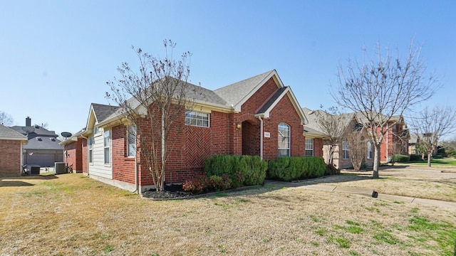 view of front of property featuring brick siding, central air condition unit, a front yard, and a shingled roof