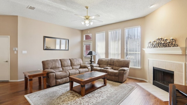 living area featuring visible vents, a tiled fireplace, a ceiling fan, a textured ceiling, and wood finished floors