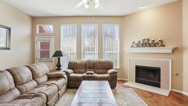 living room featuring a textured ceiling, a ceiling fan, wood finished floors, and a tile fireplace