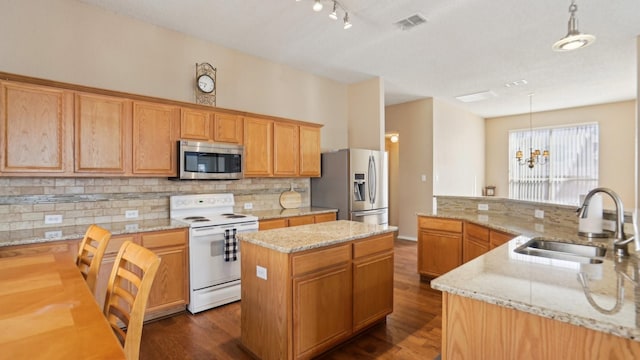 kitchen featuring appliances with stainless steel finishes, a kitchen island, a sink, backsplash, and a chandelier