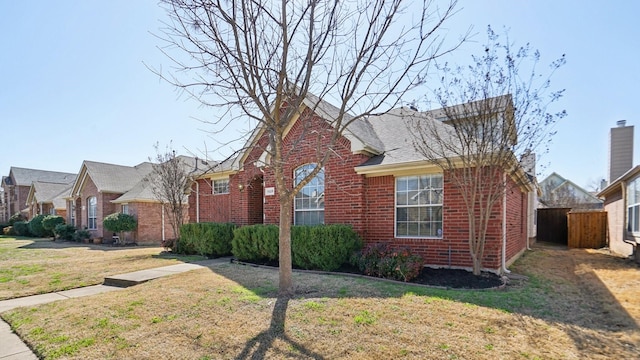 view of front facade with a front yard, fence, brick siding, and a shingled roof