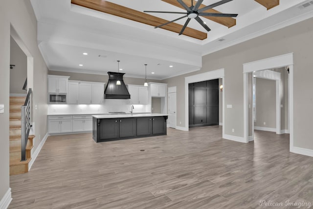 kitchen featuring decorative light fixtures, premium range hood, white cabinetry, light countertops, and a center island with sink