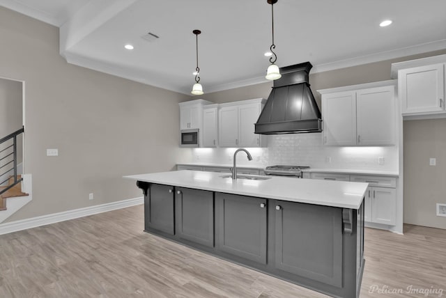 kitchen with an island with sink, custom range hood, light countertops, and a sink