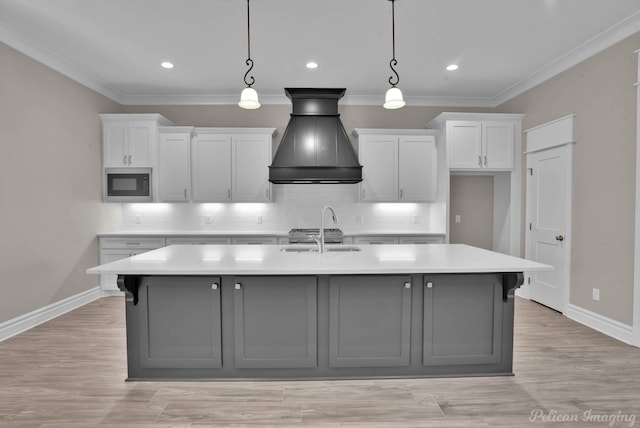 kitchen with a center island with sink, built in microwave, light countertops, white cabinetry, and pendant lighting