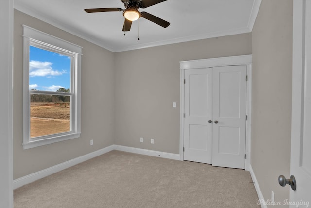 unfurnished bedroom featuring crown molding, a closet, light colored carpet, a ceiling fan, and baseboards