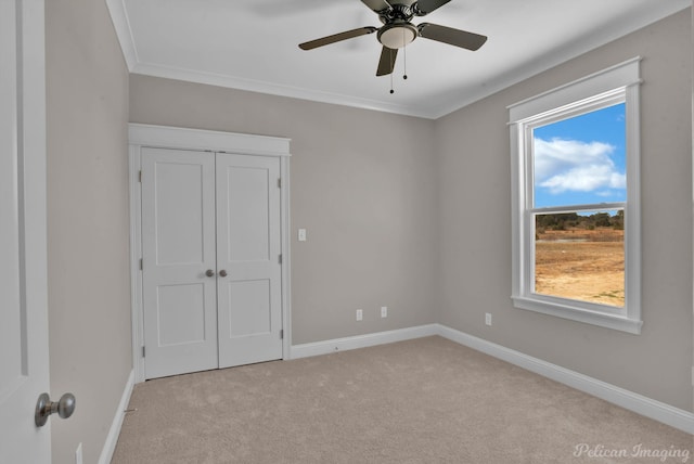 unfurnished bedroom with ceiling fan, light carpet, baseboards, a closet, and crown molding