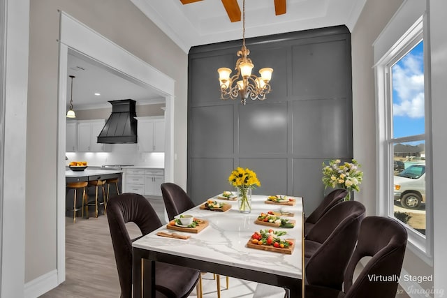 dining room featuring crown molding, a notable chandelier, a decorative wall, and light wood-style flooring