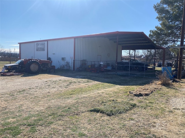 view of pole building with dirt driveway, fence, and a carport