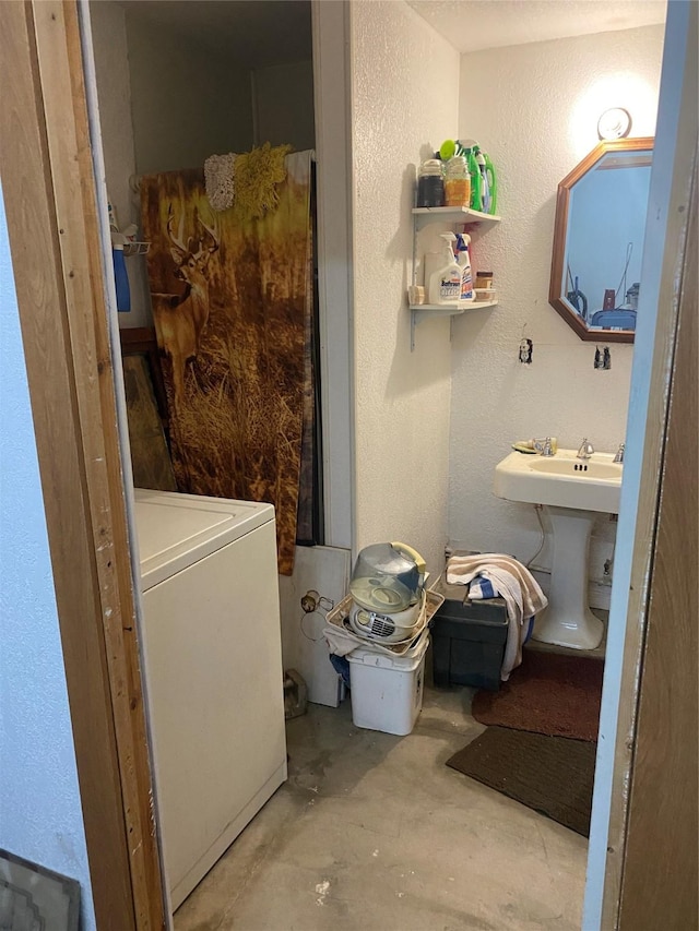 bathroom featuring concrete flooring, a textured wall, washer / clothes dryer, and a sink