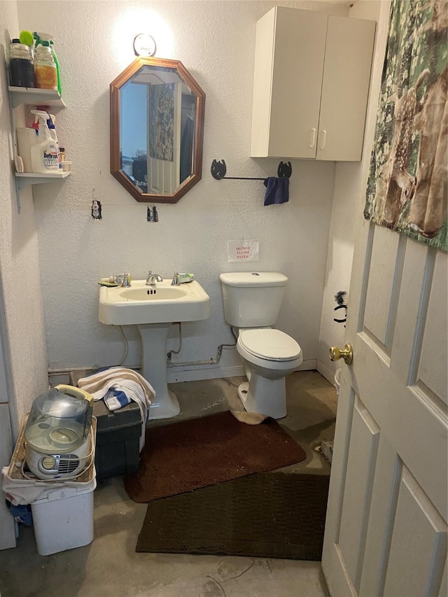 bathroom with toilet, concrete floors, and a textured wall