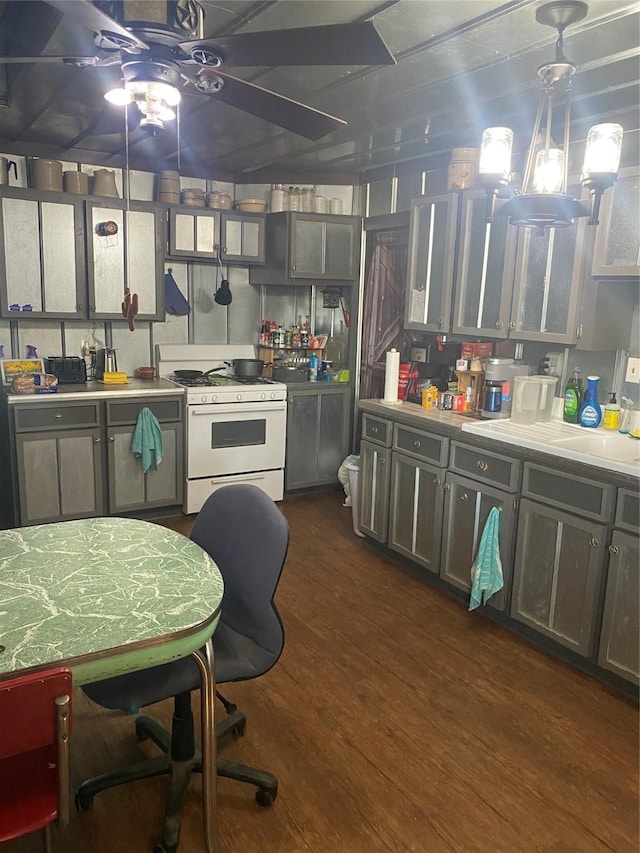 kitchen with dark wood-type flooring, hanging light fixtures, light countertops, white gas stove, and a sink