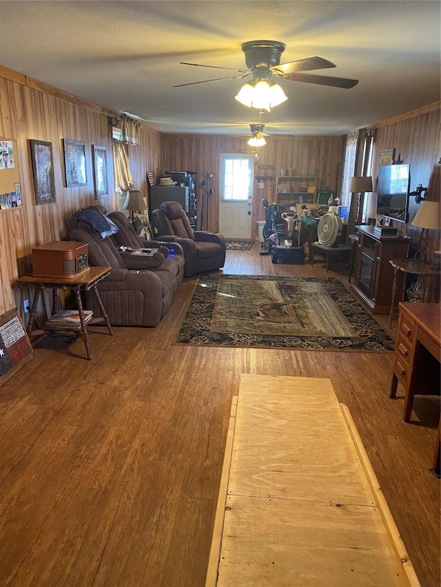 living area with ceiling fan, wooden walls, and wood finished floors