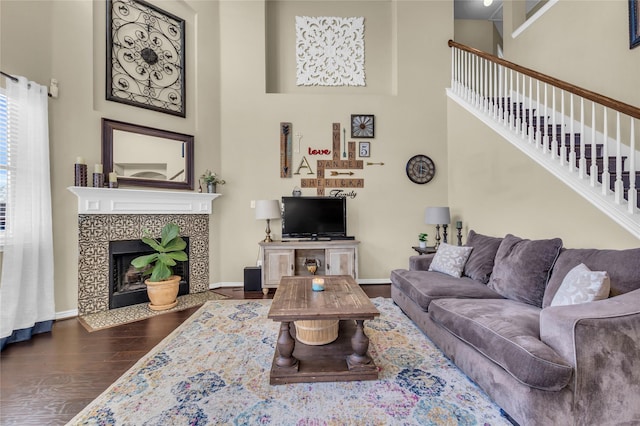 living room featuring dark wood-style flooring, a tiled fireplace, a towering ceiling, and baseboards