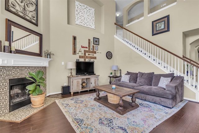 living area featuring stairs, baseboards, dark wood finished floors, and a tiled fireplace