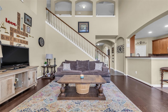 living area featuring arched walkways, dark wood-style flooring, stairway, and baseboards