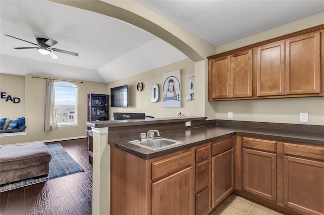 kitchen featuring a peninsula, a sink, open floor plan, brown cabinets, and dark countertops