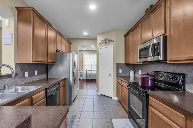 kitchen with arched walkways, a sink, dark countertops, and black appliances