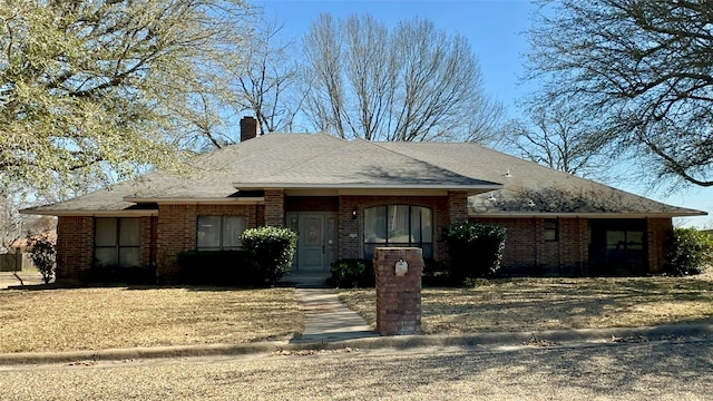 view of front of home with roof with shingles, brick siding, and a chimney