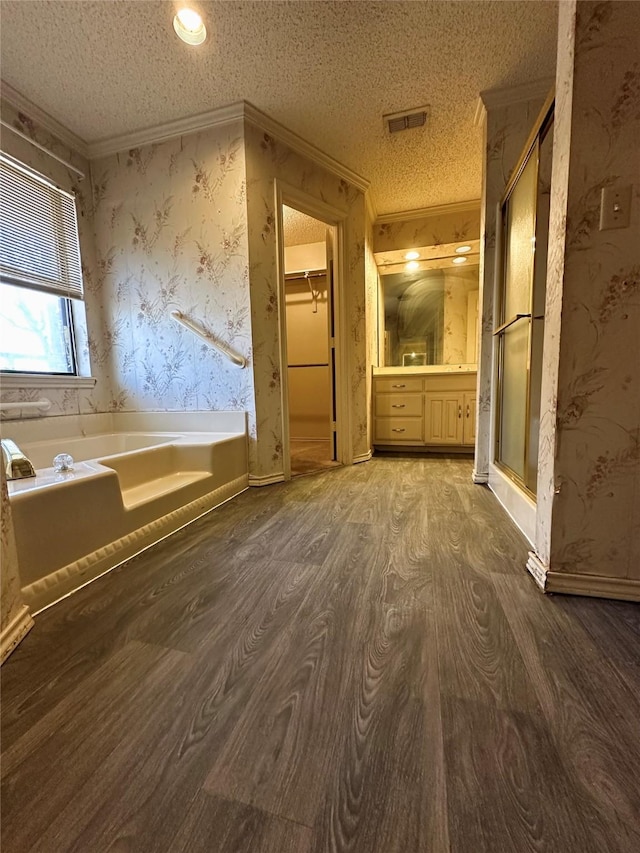 bathroom with a textured ceiling, visible vents, a walk in closet, and wood finished floors