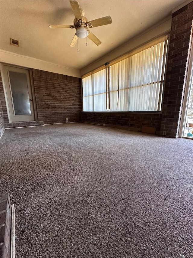 empty room featuring visible vents, a ceiling fan, brick wall, a textured ceiling, and carpet flooring