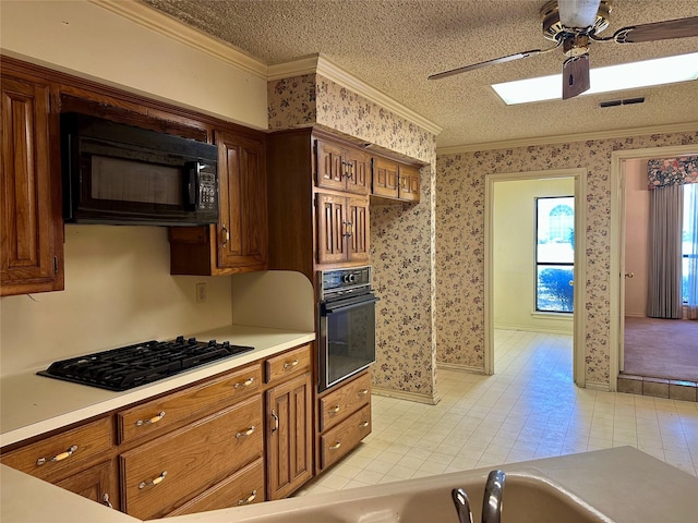 kitchen with crown molding, light countertops, a textured ceiling, black appliances, and wallpapered walls