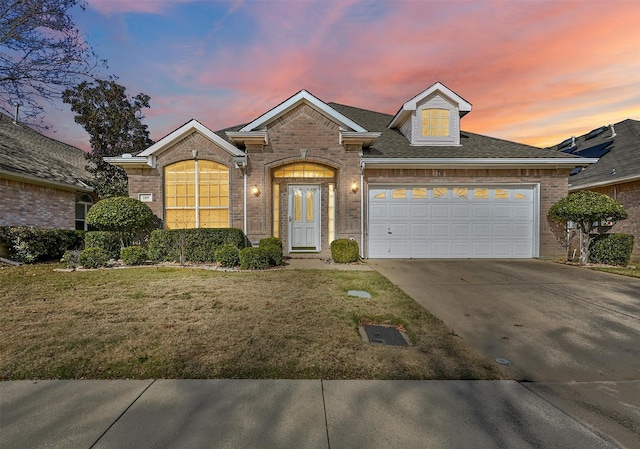 view of front facade featuring brick siding, a yard, a shingled roof, concrete driveway, and a garage