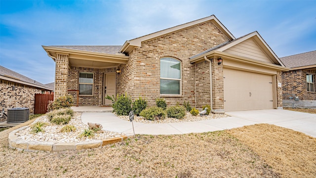 ranch-style home featuring a garage, driveway, central AC unit, roof with shingles, and brick siding