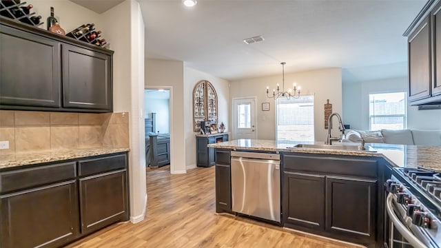 kitchen with light wood finished floors, decorative backsplash, appliances with stainless steel finishes, dark brown cabinets, and a sink