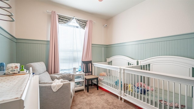 bedroom featuring a wainscoted wall, a nursery area, multiple windows, and carpet flooring