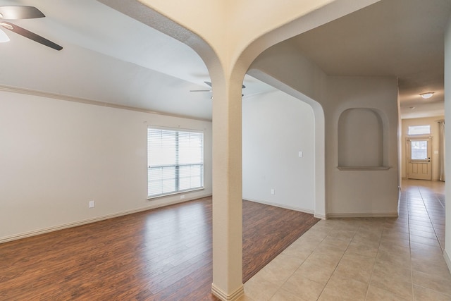 spare room with a healthy amount of sunlight, light wood-type flooring, arched walkways, and a ceiling fan