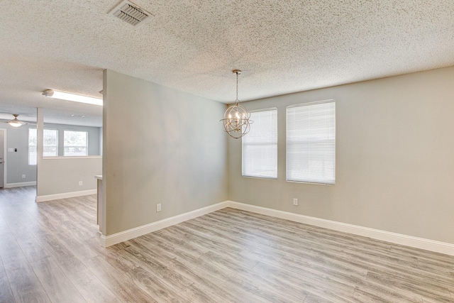 empty room featuring light wood finished floors, visible vents, a textured ceiling, baseboards, and ceiling fan with notable chandelier