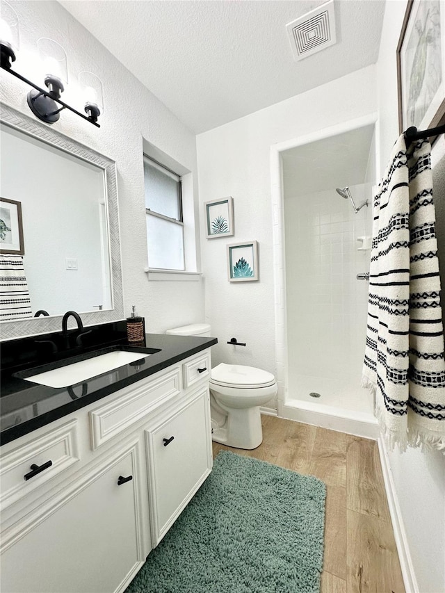 full bath featuring a textured ceiling, wood finished floors, vanity, visible vents, and a shower stall