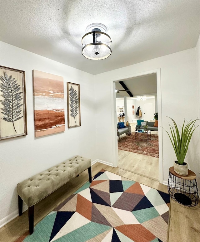 corridor featuring a textured ceiling, wood finished floors, and baseboards