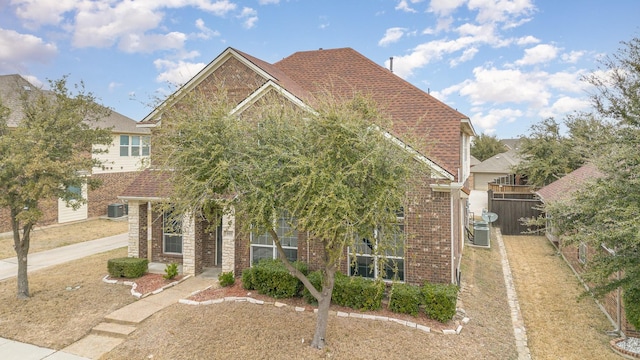 view of property hidden behind natural elements featuring brick siding, a shingled roof, and fence