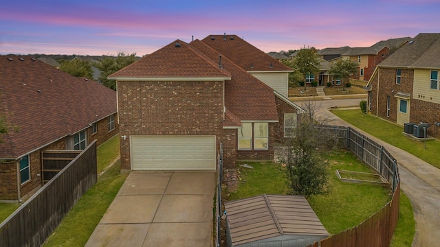 traditional-style house featuring a lawn, concrete driveway, a residential view, fence, and brick siding