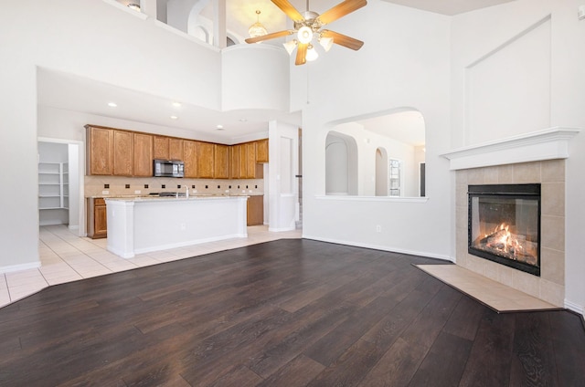 unfurnished living room featuring a ceiling fan, baseboards, a fireplace, and light wood finished floors