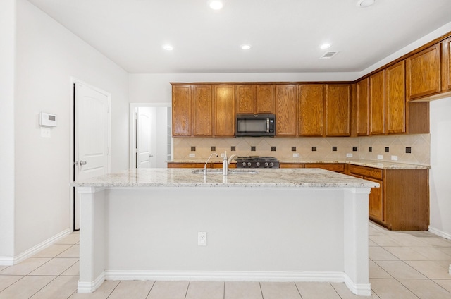 kitchen featuring brown cabinets, a kitchen island with sink, stainless steel microwave, and a sink